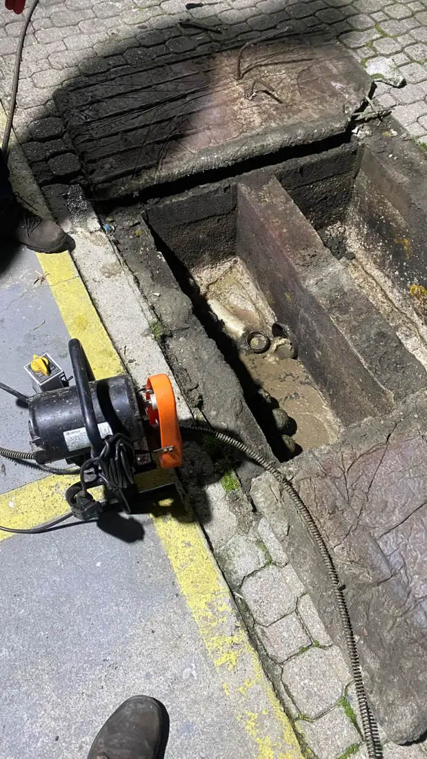 Máquina desentupidora profissional da D.Lucca ao lado de uma caixa de passagem aberta