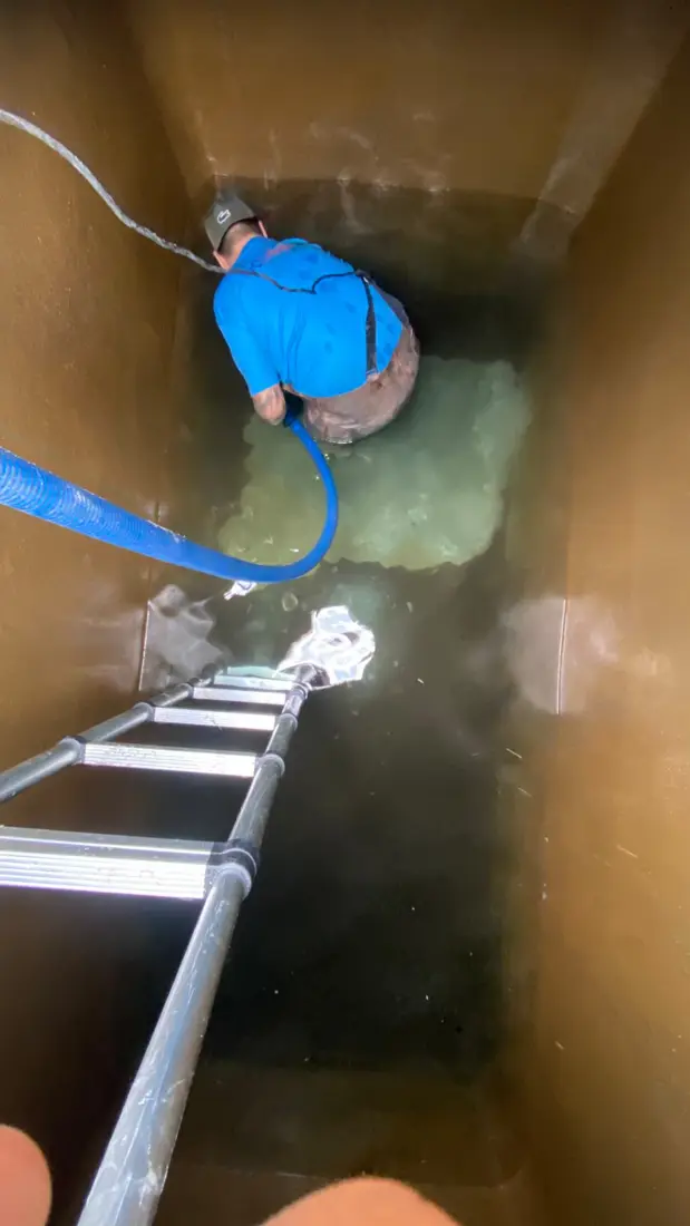 Vista de cima de técnico da D.Lucca higienizando reservatório com escada de acesso